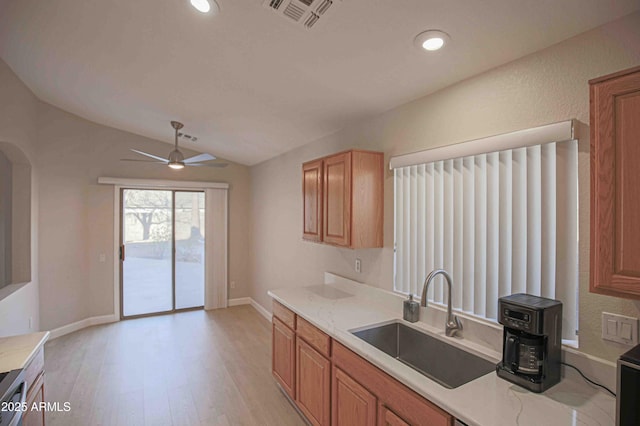 kitchen with lofted ceiling, light hardwood / wood-style floors, sink, ceiling fan, and light stone counters