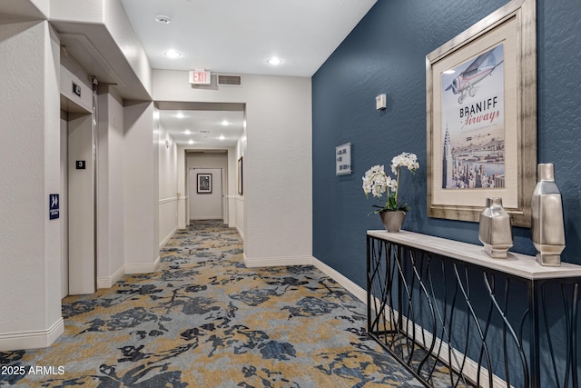 hallway with elevator, baseboards, and a textured wall