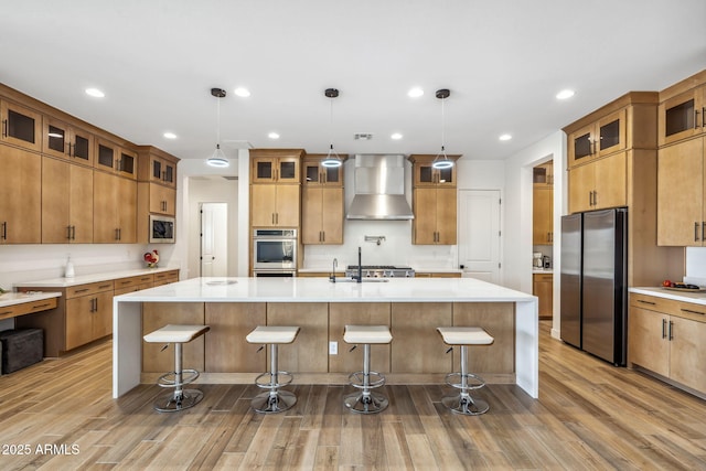 kitchen featuring wall chimney range hood, light countertops, stainless steel appliances, and wood finished floors