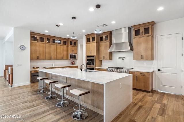 kitchen featuring brown cabinetry, visible vents, appliances with stainless steel finishes, wall chimney exhaust hood, and light wood-style flooring