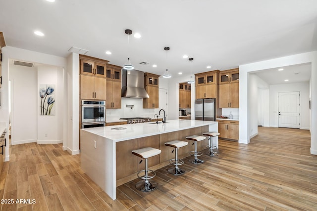 kitchen with visible vents, appliances with stainless steel finishes, light wood-style flooring, and wall chimney exhaust hood