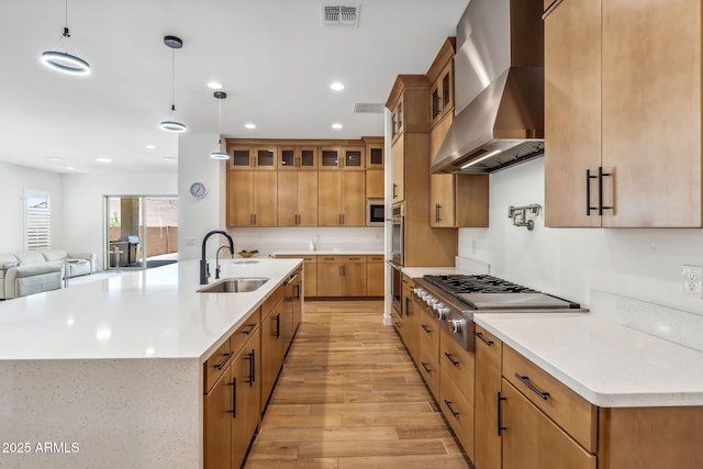 kitchen featuring visible vents, open floor plan, wall chimney exhaust hood, a sink, and stainless steel appliances