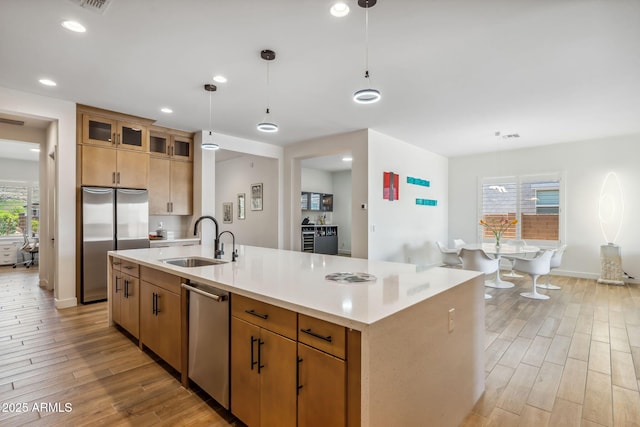 kitchen featuring a sink, light wood finished floors, light countertops, stainless steel appliances, and decorative light fixtures