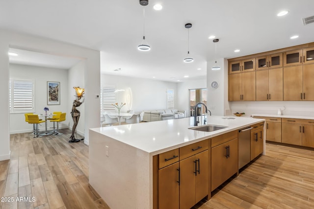 kitchen with stainless steel dishwasher, a sink, light wood finished floors, and light countertops
