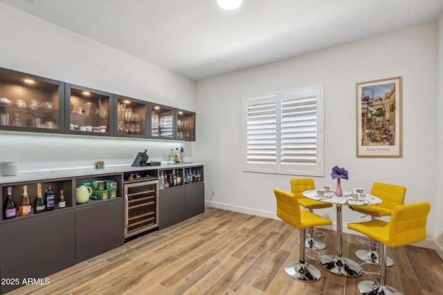 bar with beverage cooler, light wood finished floors, baseboards, and indoor bar