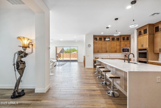 kitchen with appliances with stainless steel finishes, a sink, light wood finished floors, brown cabinetry, and visible vents