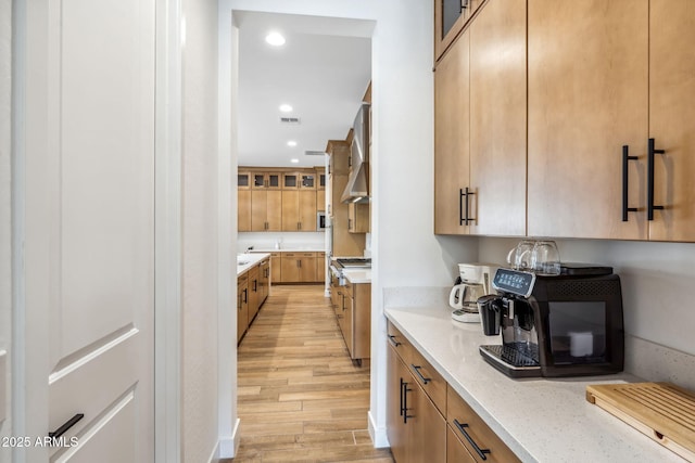 kitchen with stainless steel gas range, light stone counters, light wood finished floors, recessed lighting, and visible vents