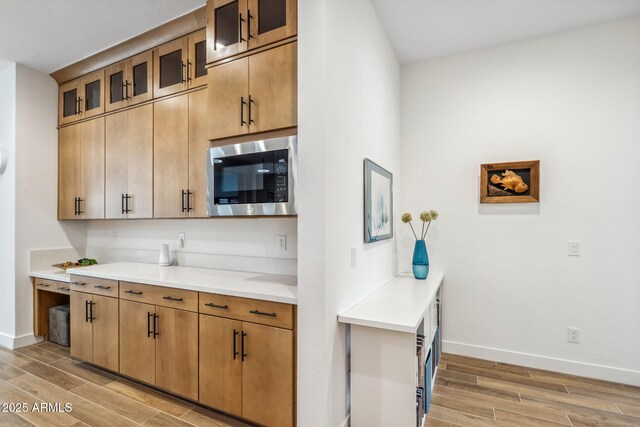 kitchen with baseboards, wood tiled floor, stainless steel microwave, and light countertops