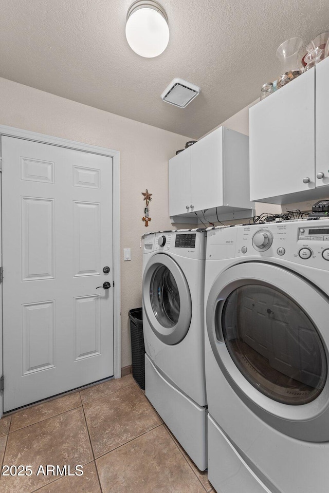 laundry room featuring washer and dryer, light tile patterned floors, cabinets, and a textured ceiling