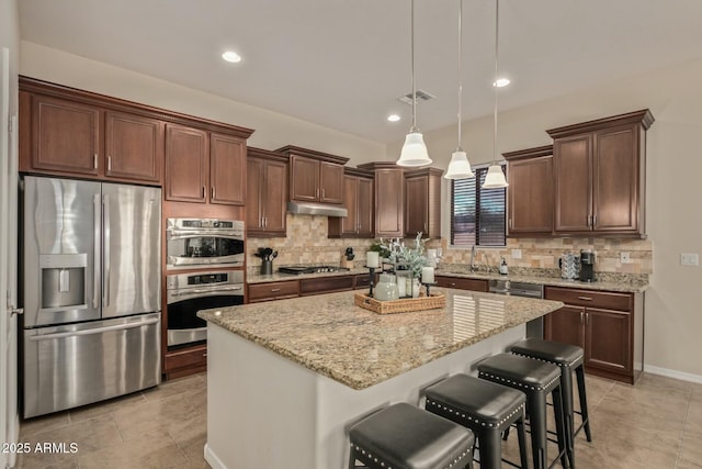 kitchen with a center island, hanging light fixtures, light stone countertops, appliances with stainless steel finishes, and a breakfast bar area