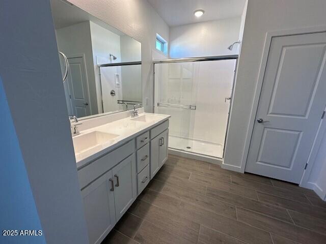 bathroom featuring double vanity, a shower stall, wood tiled floor, and a sink