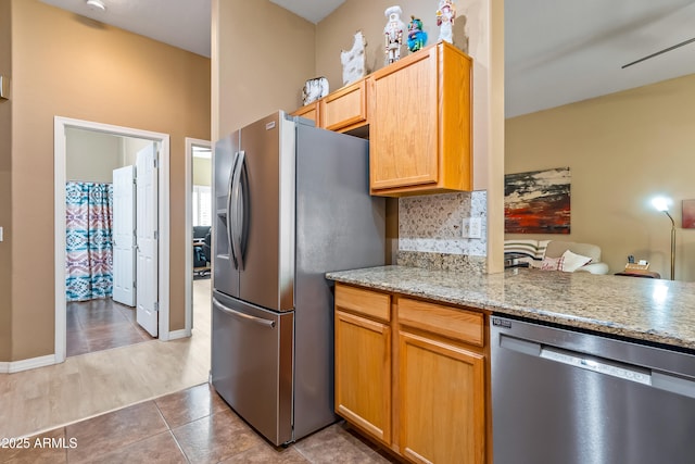 kitchen featuring appliances with stainless steel finishes, decorative backsplash, tile patterned flooring, kitchen peninsula, and light stone countertops