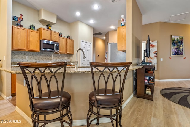 kitchen featuring stainless steel appliances, light stone countertops, a breakfast bar area, and kitchen peninsula