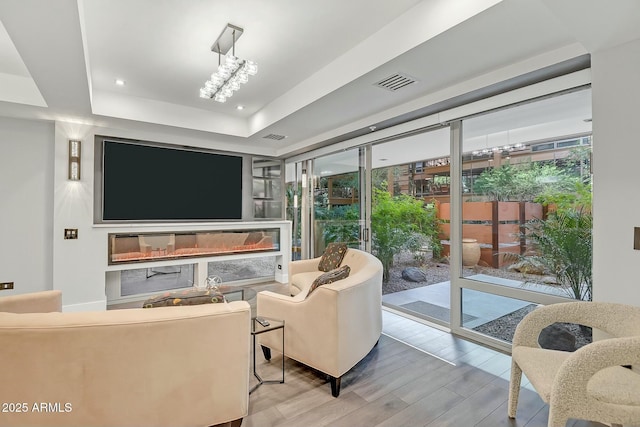 living room with visible vents, a raised ceiling, a glass covered fireplace, and wood finished floors