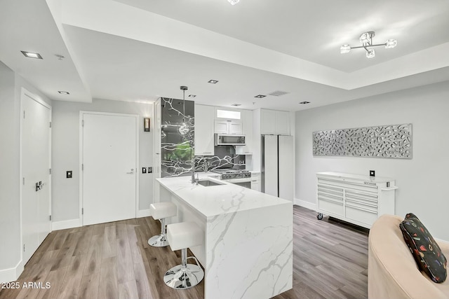 kitchen with stainless steel microwave, wood finished floors, freestanding refrigerator, range, and light stone countertops