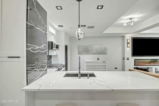 kitchen with stainless steel microwave, visible vents, light stone countertops, white cabinets, and a sink