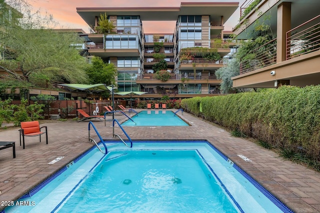 pool at dusk with a patio area, a community pool, a community hot tub, and fence