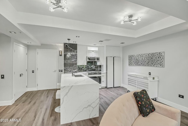 kitchen featuring a sink, stainless steel appliances, a raised ceiling, and light wood-style floors