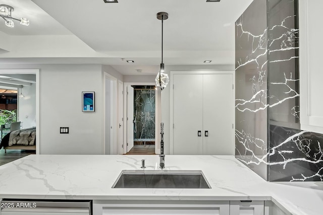 kitchen with pendant lighting, a sink, white cabinetry, light stone countertops, and dishwasher