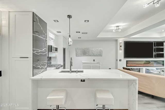 kitchen featuring a sink, stainless steel microwave, light stone counters, and a peninsula