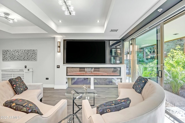 living room with wood finished floors, visible vents, baseboards, a tray ceiling, and recessed lighting