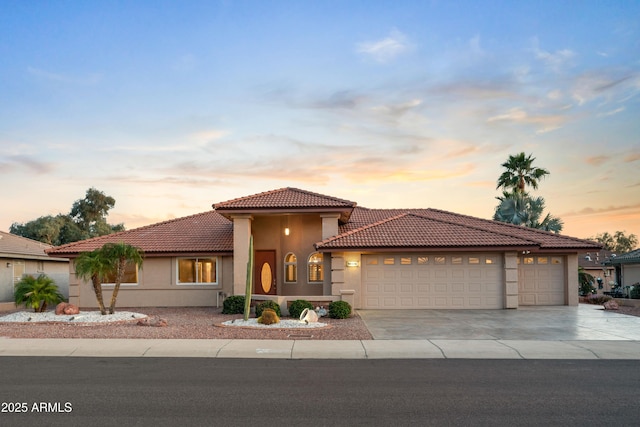 mediterranean / spanish house featuring stucco siding, a tiled roof, concrete driveway, and a garage