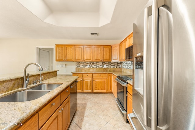 kitchen with a sink, light stone counters, tasteful backsplash, stainless steel appliances, and a raised ceiling