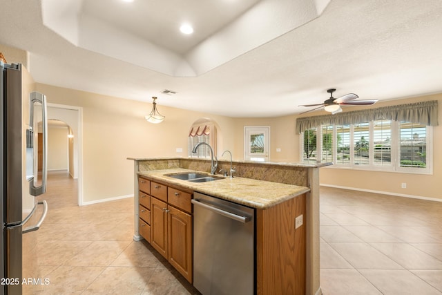 kitchen with light tile patterned floors, appliances with stainless steel finishes, arched walkways, a raised ceiling, and a sink