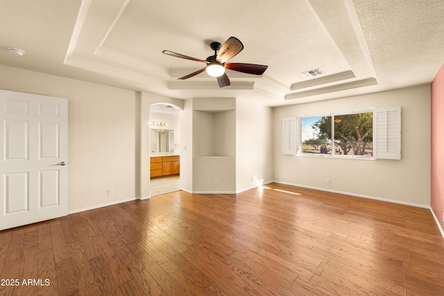 interior space with light wood-type flooring, a tray ceiling, arched walkways, and visible vents