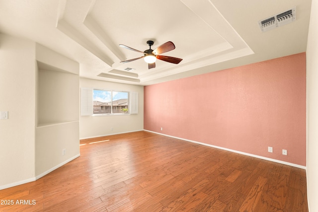 unfurnished room featuring a tray ceiling, baseboards, visible vents, and wood finished floors