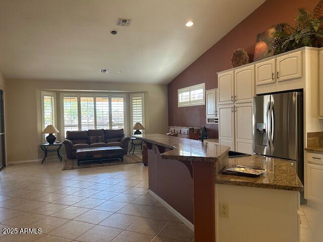 kitchen with stainless steel refrigerator with ice dispenser, light tile patterned floors, visible vents, open floor plan, and dark stone counters