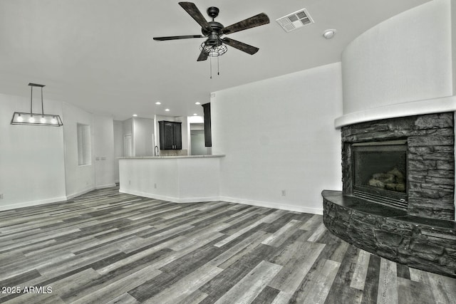 unfurnished living room with ceiling fan, dark wood-type flooring, and a stone fireplace