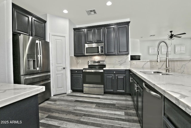 kitchen with light stone countertops, dark hardwood / wood-style floors, appliances with stainless steel finishes, ceiling fan, and sink