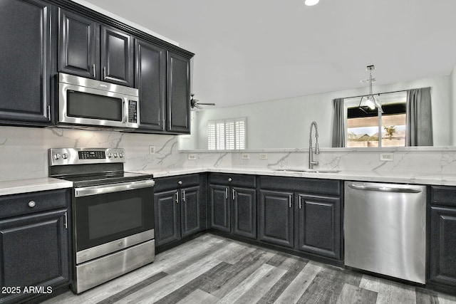 kitchen with light hardwood / wood-style floors, stainless steel appliances, ceiling fan, sink, and backsplash