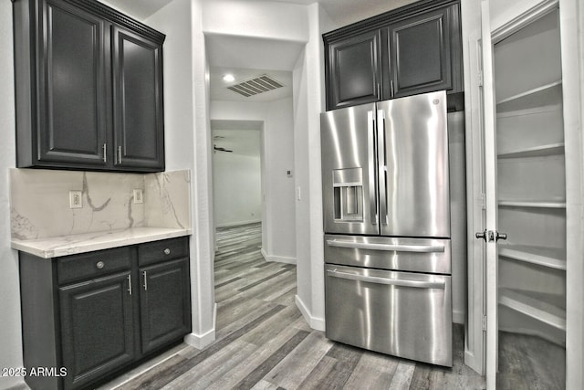 kitchen with light stone countertops, tasteful backsplash, stainless steel refrigerator with ice dispenser, and hardwood / wood-style flooring