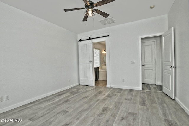 unfurnished bedroom featuring connected bathroom, ceiling fan, a barn door, and light hardwood / wood-style flooring