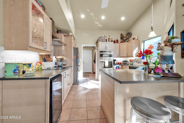 kitchen featuring beverage cooler, decorative light fixtures, a kitchen bar, light brown cabinetry, and appliances with stainless steel finishes