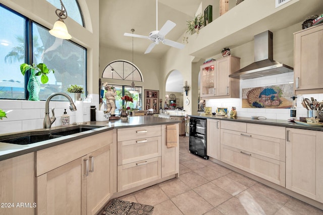 kitchen featuring wall chimney exhaust hood, sink, pendant lighting, high vaulted ceiling, and wine cooler