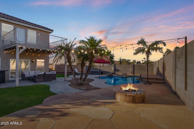 pool at dusk with an outdoor living space with a fire pit and a patio