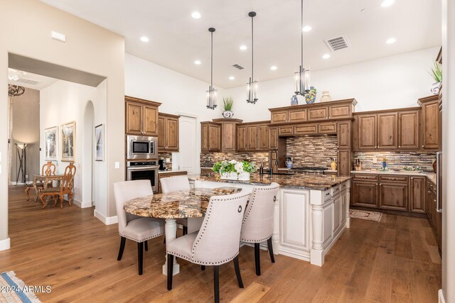 kitchen featuring an island with sink, dark stone counters, hardwood / wood-style floors, and appliances with stainless steel finishes