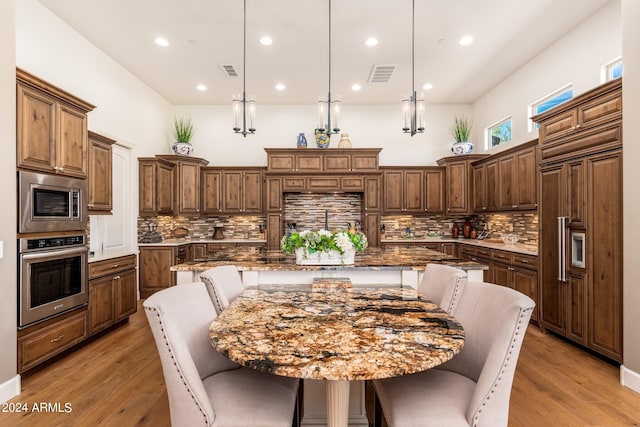 kitchen with a large island, light wood-type flooring, pendant lighting, built in appliances, and backsplash