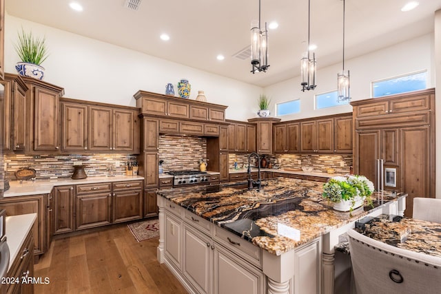 kitchen featuring a center island with sink, backsplash, pendant lighting, and light stone counters