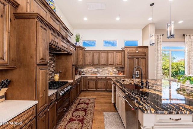 kitchen with pendant lighting, light hardwood / wood-style floors, sink, backsplash, and appliances with stainless steel finishes