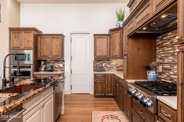 kitchen with dark stone counters, light wood-type flooring, decorative backsplash, stainless steel appliances, and premium range hood