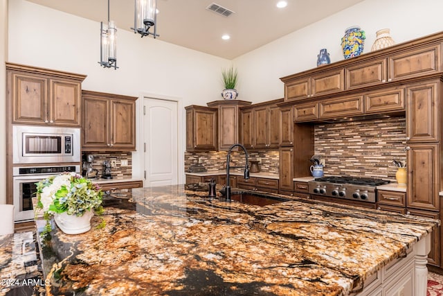 kitchen with pendant lighting, sink, backsplash, stainless steel appliances, and dark stone counters