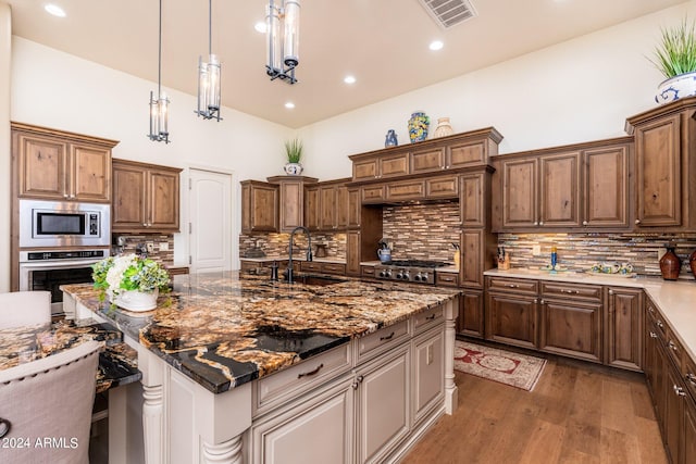 kitchen featuring appliances with stainless steel finishes, dark wood-type flooring, tasteful backsplash, decorative light fixtures, and sink