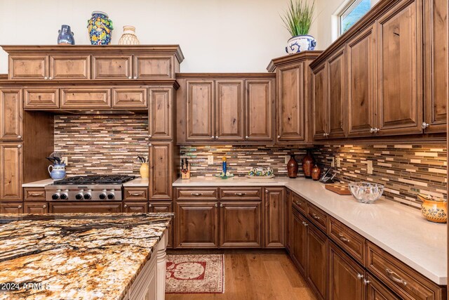 kitchen with light stone countertops, light wood-type flooring, backsplash, and stainless steel gas cooktop