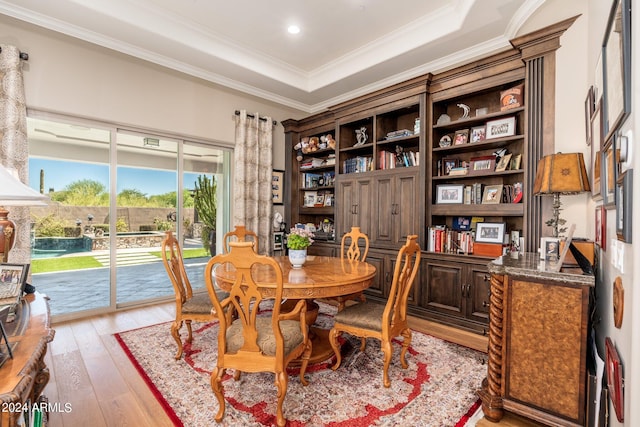 dining space with ornamental molding, a raised ceiling, and light hardwood / wood-style floors