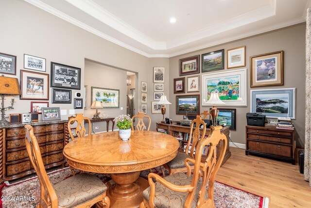 dining space with light wood-type flooring, a raised ceiling, and crown molding