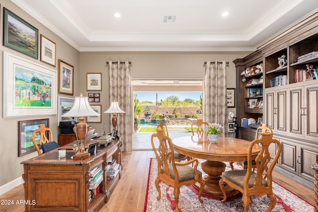 dining space with a raised ceiling, crown molding, and light hardwood / wood-style floors